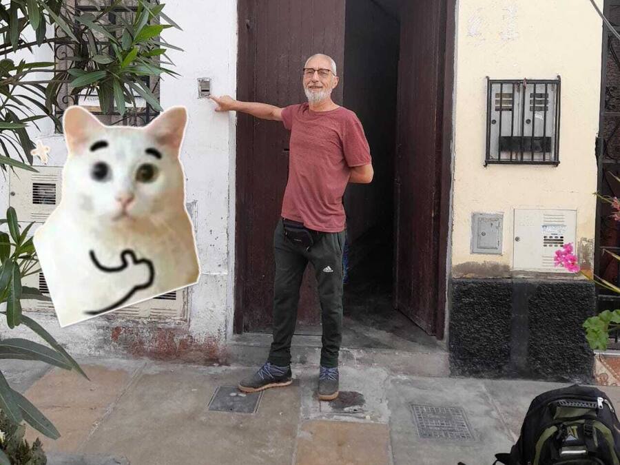 Un hombre de pie frente a un edificio con una puerta, un ventanal y una planta pequeña.