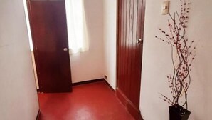 Un pasillo estrecho con piso rojo, una puerta de madera y un aplique en la pared.