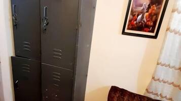 A room with a large metal wardrobe, a framed picture on the wall, and a patterned sofa.