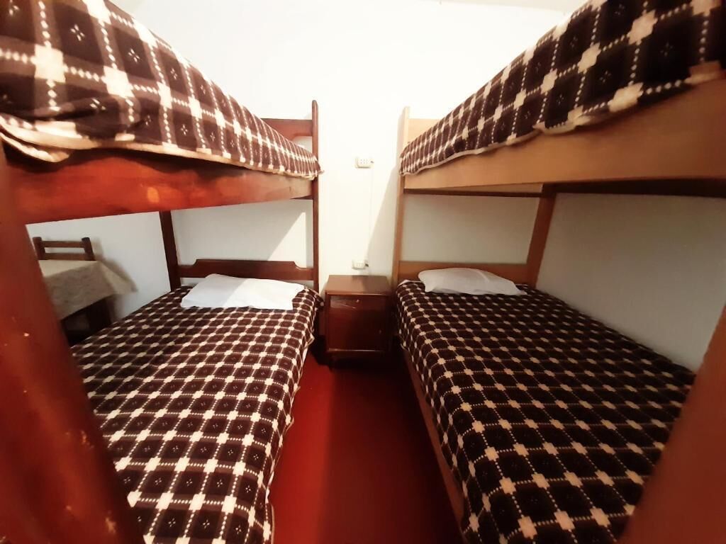 Una habitación con dos literas, cada una con un edredón a cuadros. Hay una mesita de noche de madera entre las camas.