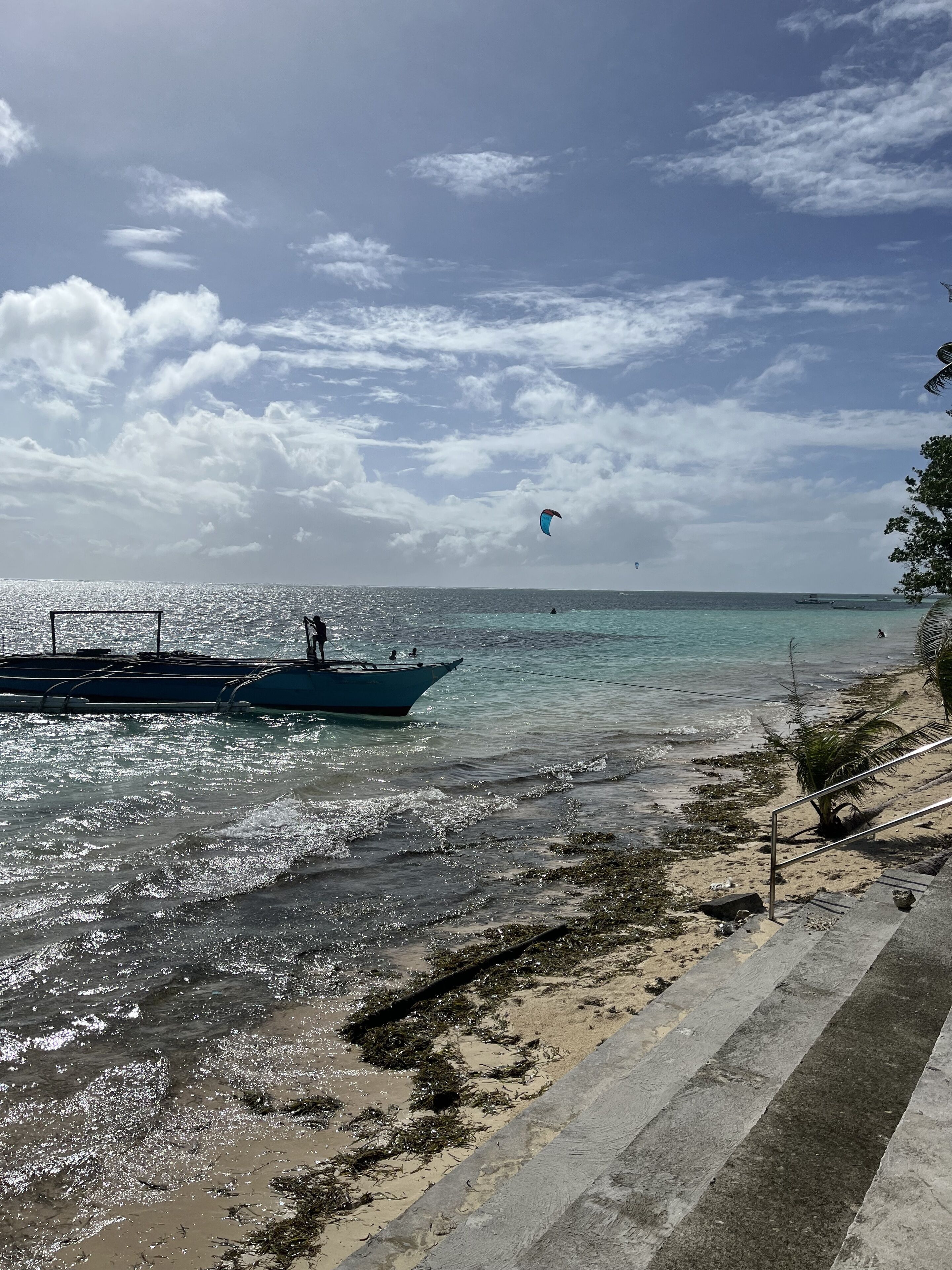 Una playa con barcos, cielo despejado y una persona volando una cometa.