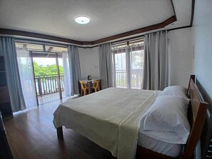 A bedroom with a large bed, a small table with chairs, and a balcony with curtains. - Takbo Beach Resort (General Luna)