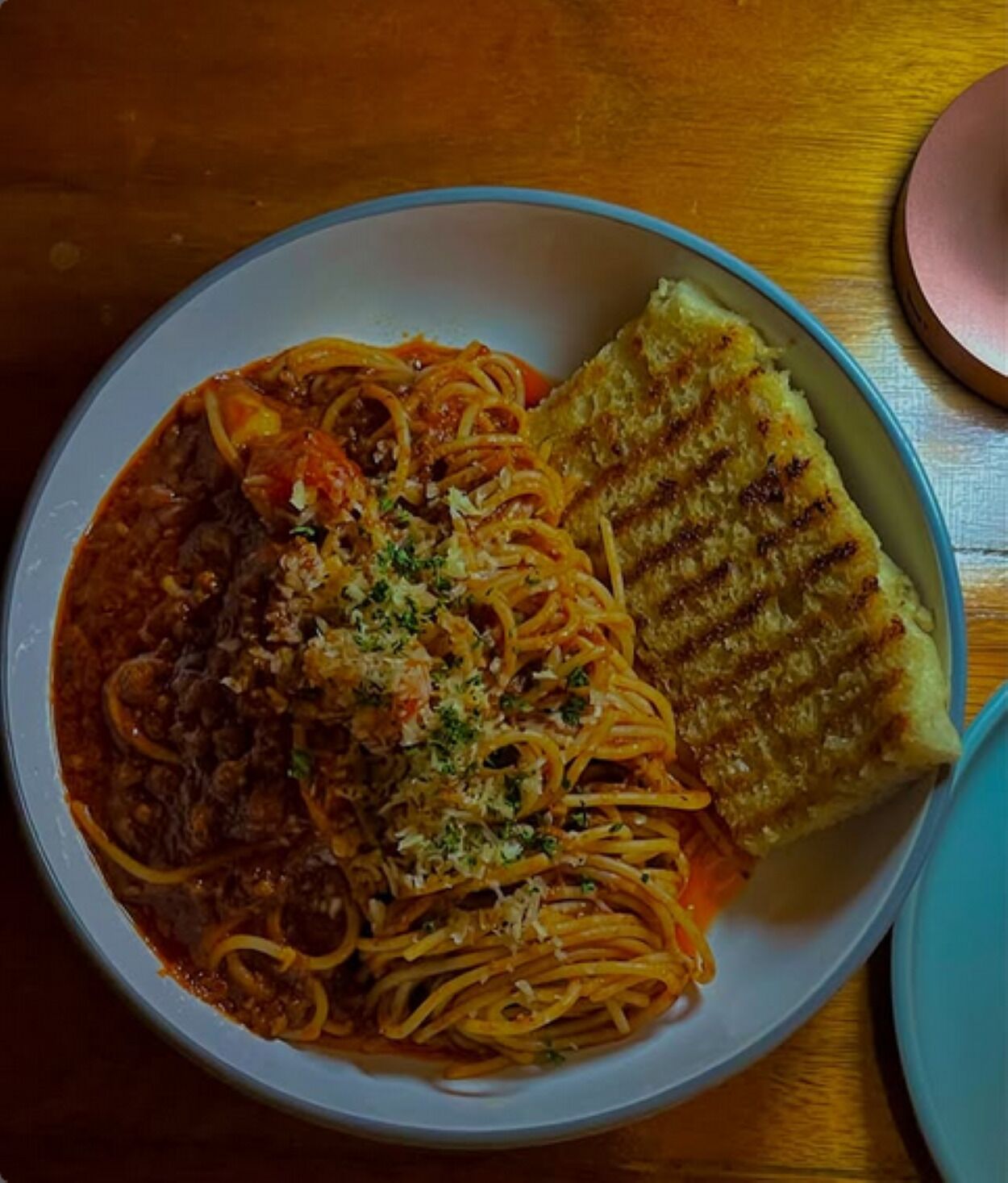 A bowl of spaghetti with meat sauce and a grilled cheese sandwich on a wooden table.