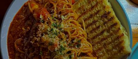 A bowl of spaghetti with meat sauce and a grilled cheese sandwich on a wooden table.