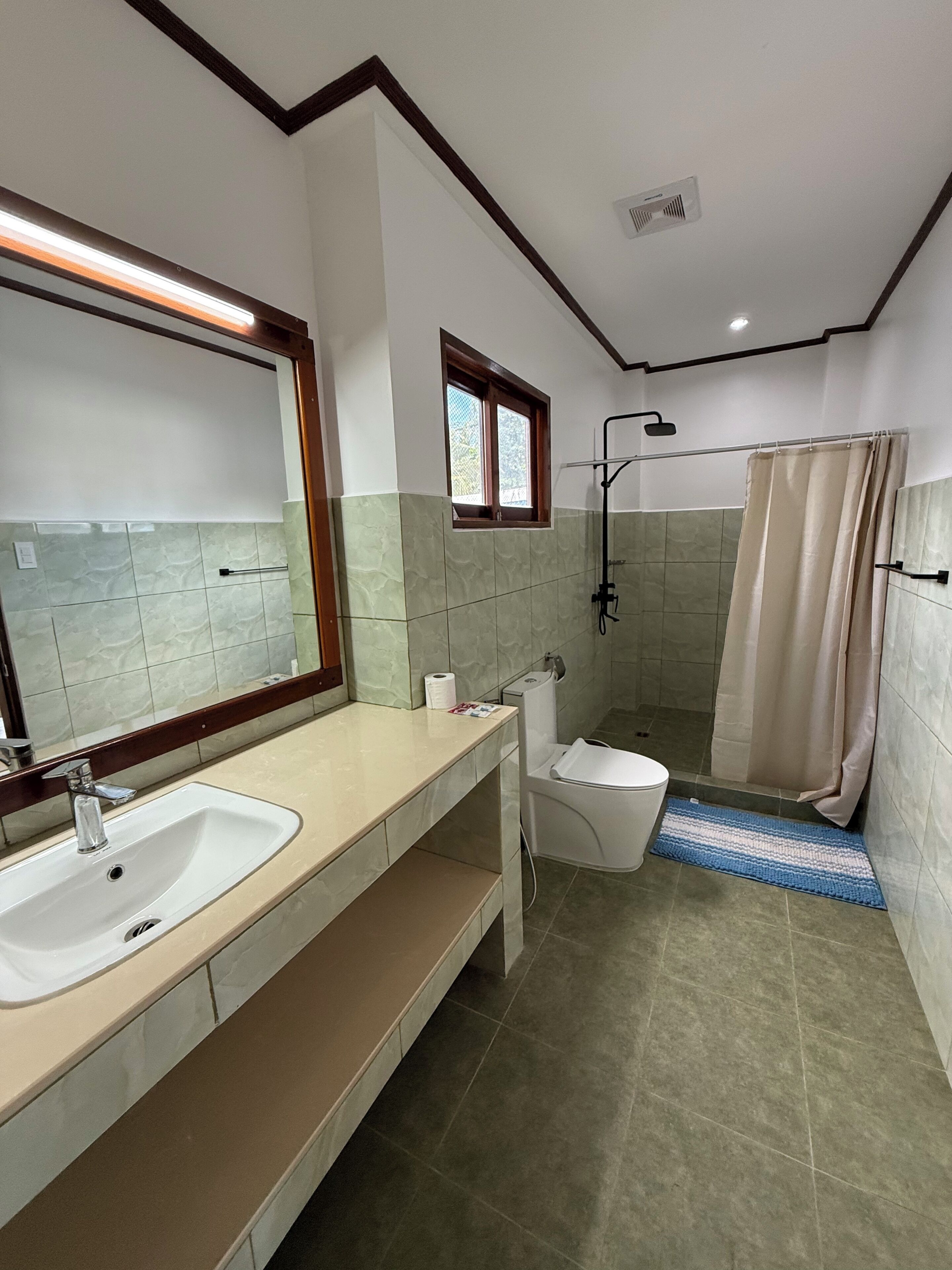A bathroom with a sink, toilet, shower, and a window.