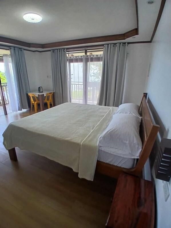 A bedroom with a large bed, wooden headboard, and a small desk with chairs. - Takbo Beach Resort (General Luna)