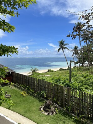 A tropical beach view with a wooden fence, lush greenery, and a clear blue sky. - Takbo Beach Resort (General Luna)