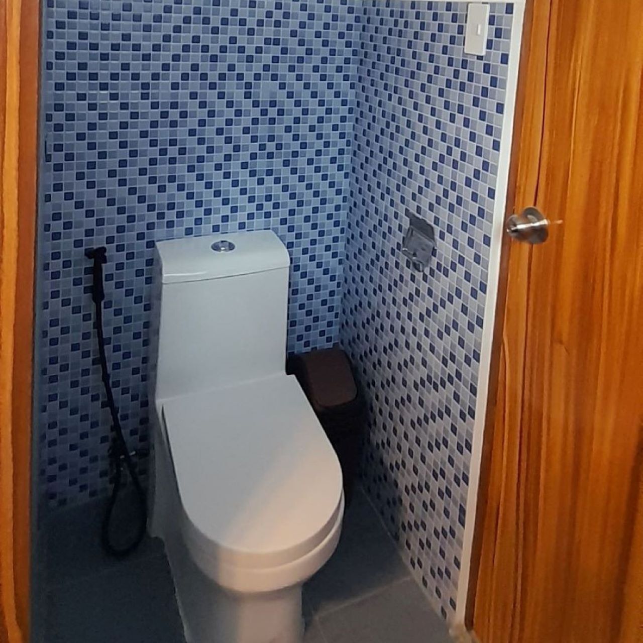 A small bathroom with a toilet, a small trash bin, and a shower area.