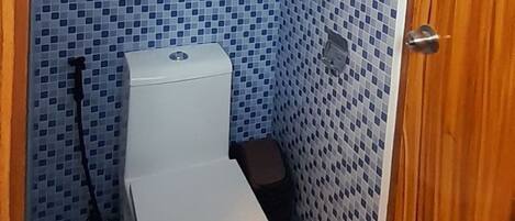 A small bathroom with a toilet, a small trash bin, and a shower area.