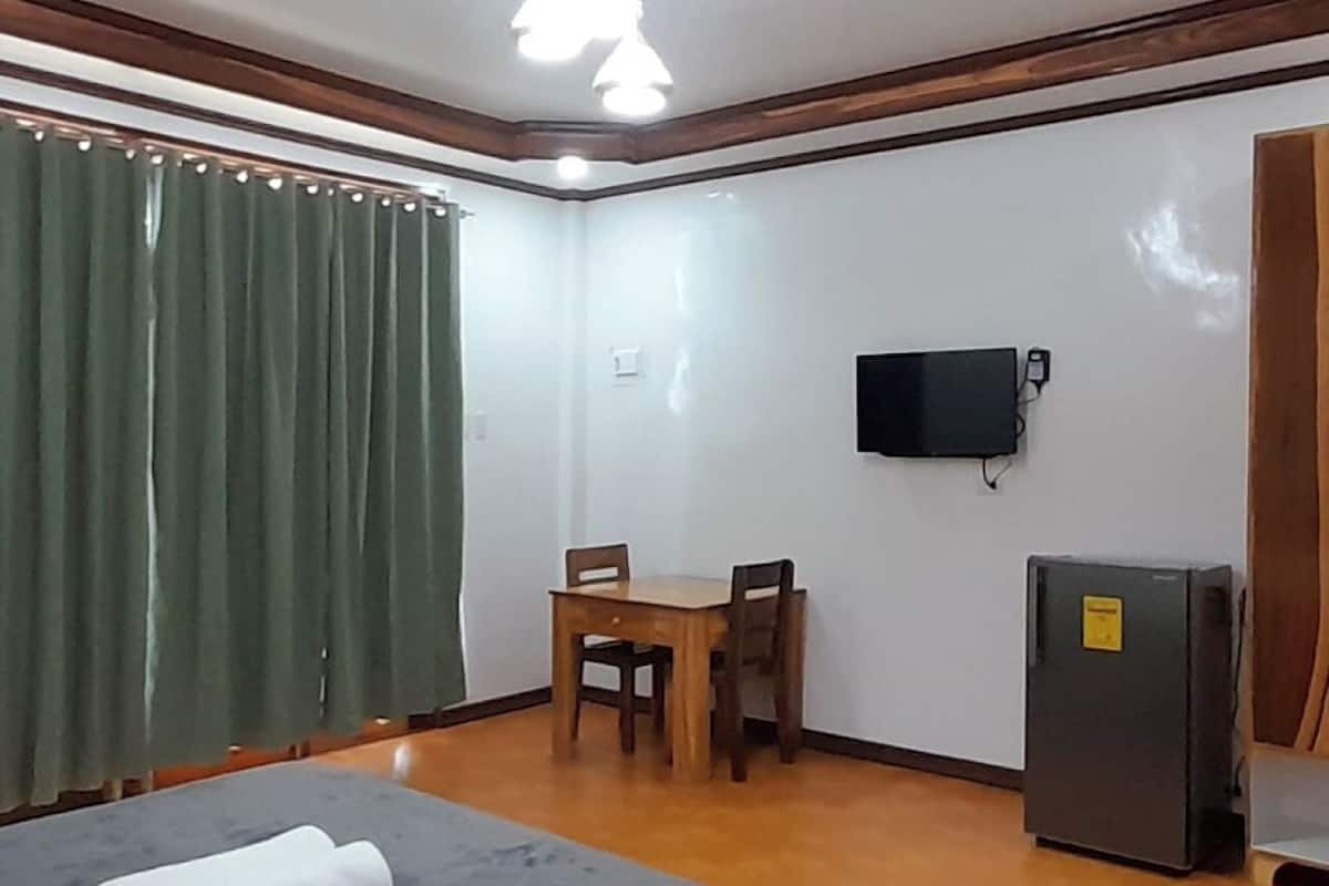 A hotel room with a bed, a small table with chairs, a television mounted on the wall, and a refrigerator.