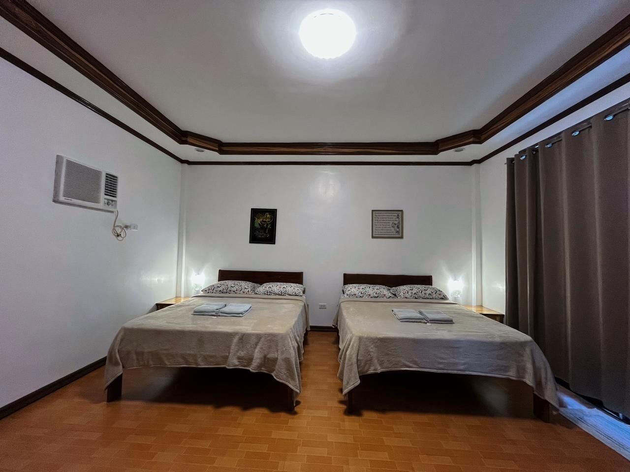 A room with two beds, a ceiling light, a vent, and a window with curtains.