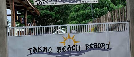A sign for Takbo Beach Resort with a sun and waves design, indicating a beach theme.