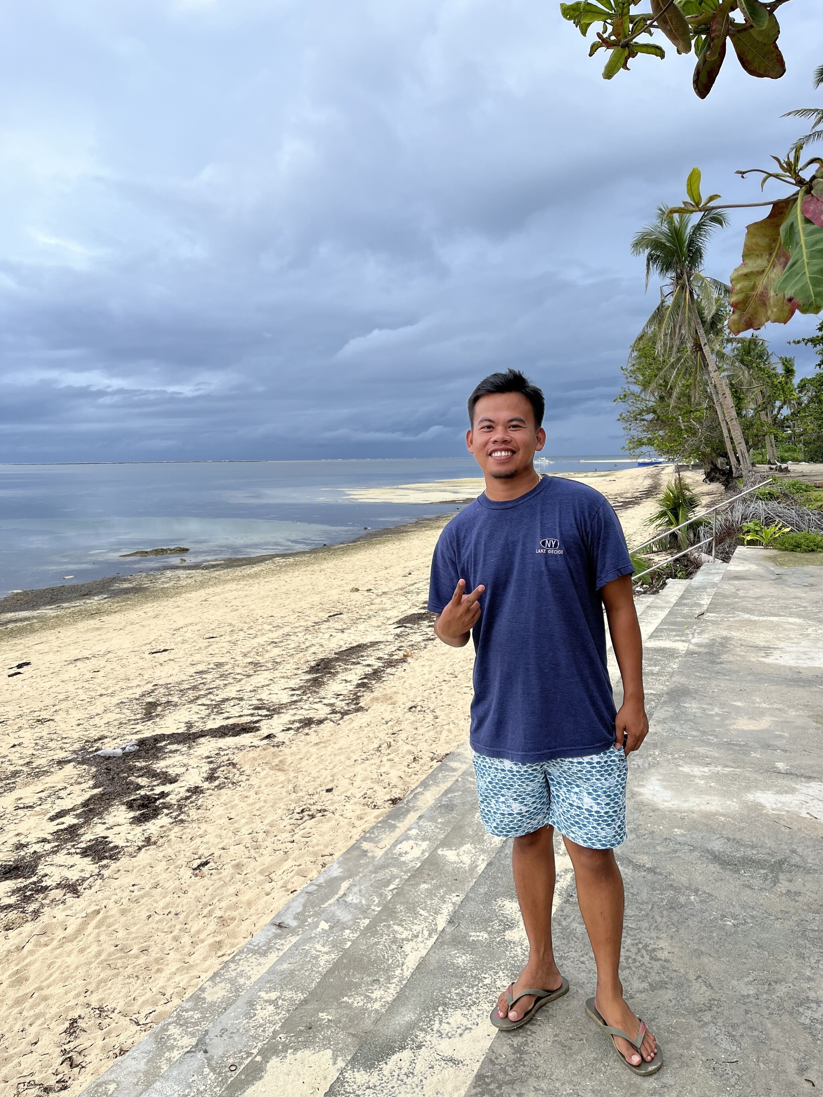 A person standing on a concrete path by a beach with a cloudy sky.