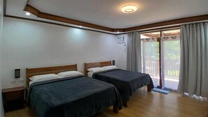 Una stanza con due letti, poggiatesta in legno, una lampada a soffitto, condizionatore d'aria e una porta scorrevole in vetro che dà sull'esterno.