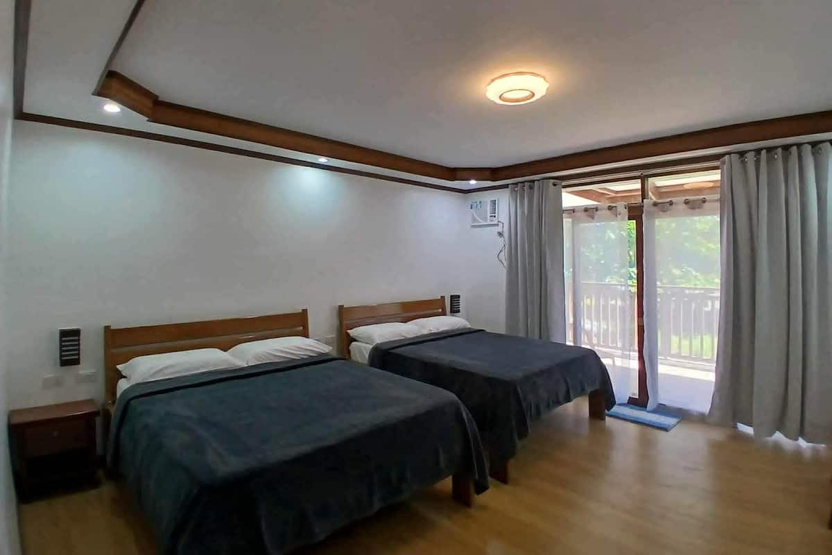 A room with two beds, wooden headboards, a ceiling light, an air conditioning unit, and a sliding glass door to the outside.