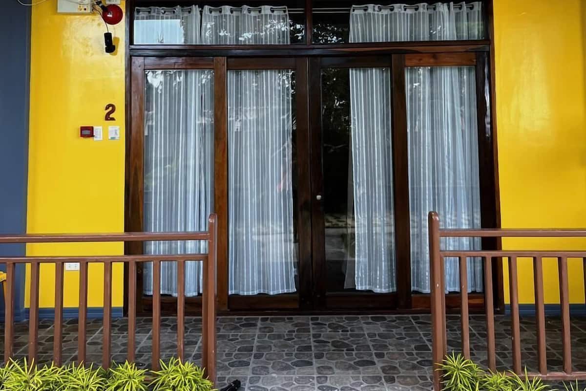 A building entrance with a yellow and blue facade, a wooden door with glass panels, and a small porch with steps and railings.