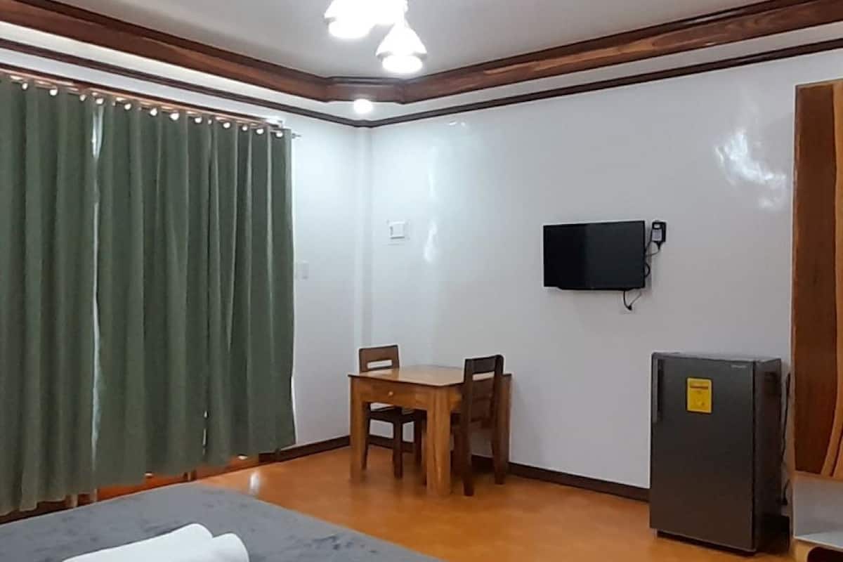 A room with a bed, a table with chairs, a television, and a refrigerator.