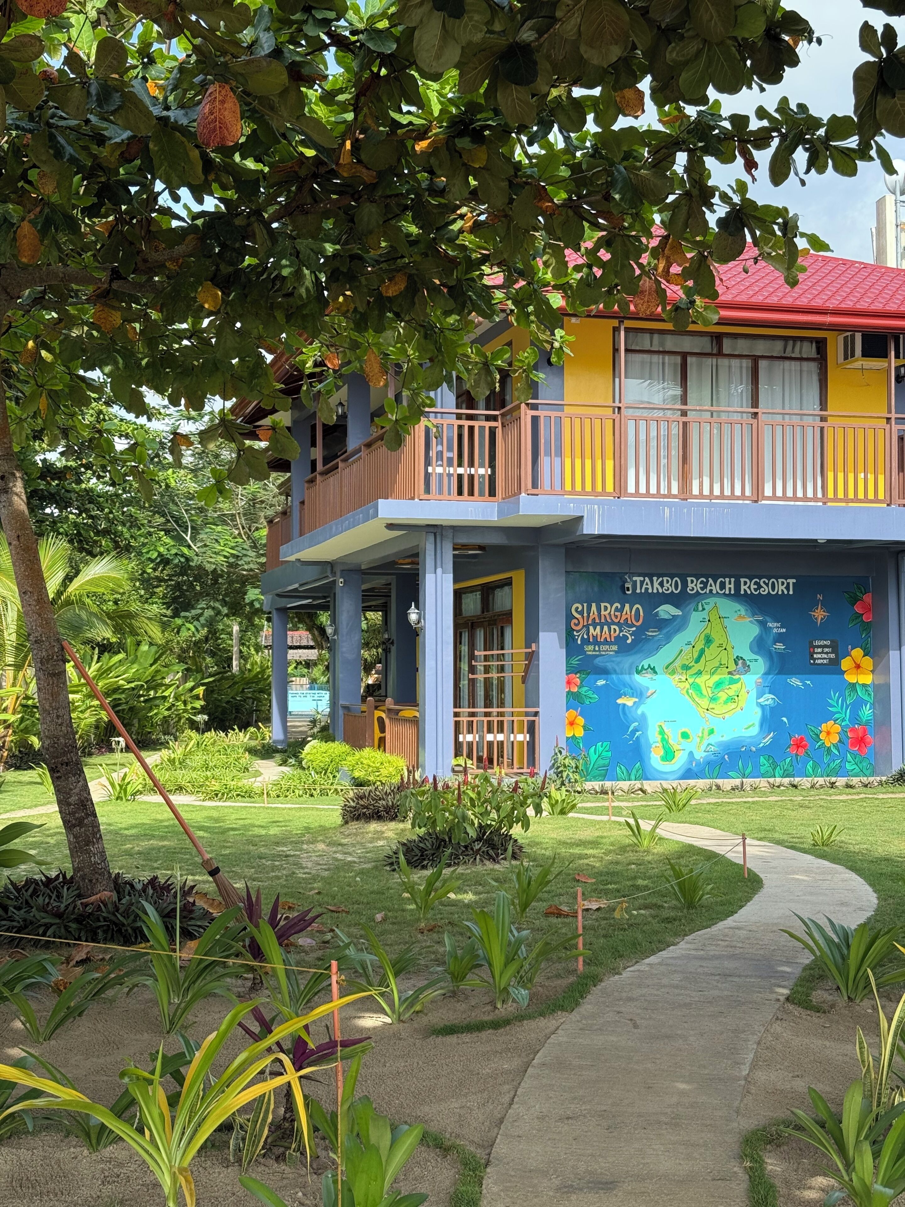 Un edificio de dos pisos con un balcón, un cartel que dice 'Takbo Beach Resort' y un mural de mapa colorido.
