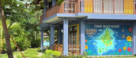 Un edificio de dos pisos con un balcón, un cartel que dice 'Takbo Beach Resort' y un mural de mapa colorido.
