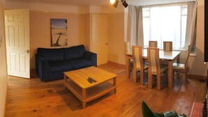 A living room with a blue sofa, a wooden coffee table, and a dining table with chairs. - Lovely 3 Bedroom Holiday Home With Free Parking (Fareham)