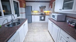 A compact kitchen with white cabinets, a stainless steel sink, a refrigerator, an oven, a microwave, and a gas stove. - Lovely 3 Bedroom Holiday Home With Free Parking (Fareham)
