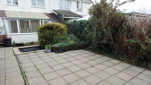 A residential backyard with a paved patio, a small garden bed, and a variety of plants and shrubs. - Lovely 3 Bedroom Holiday Home With Free Parking (Fareham)