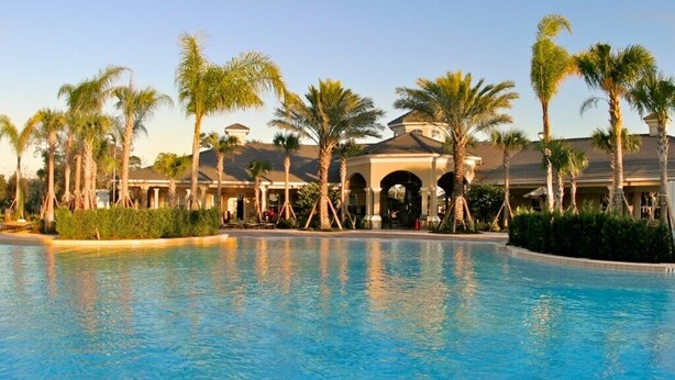 A swimming pool with a building in the background, surrounded by palm trees. - Amazing 3 Bed Condo in Windsor Hills - Close to Disney! (Kissimmee)