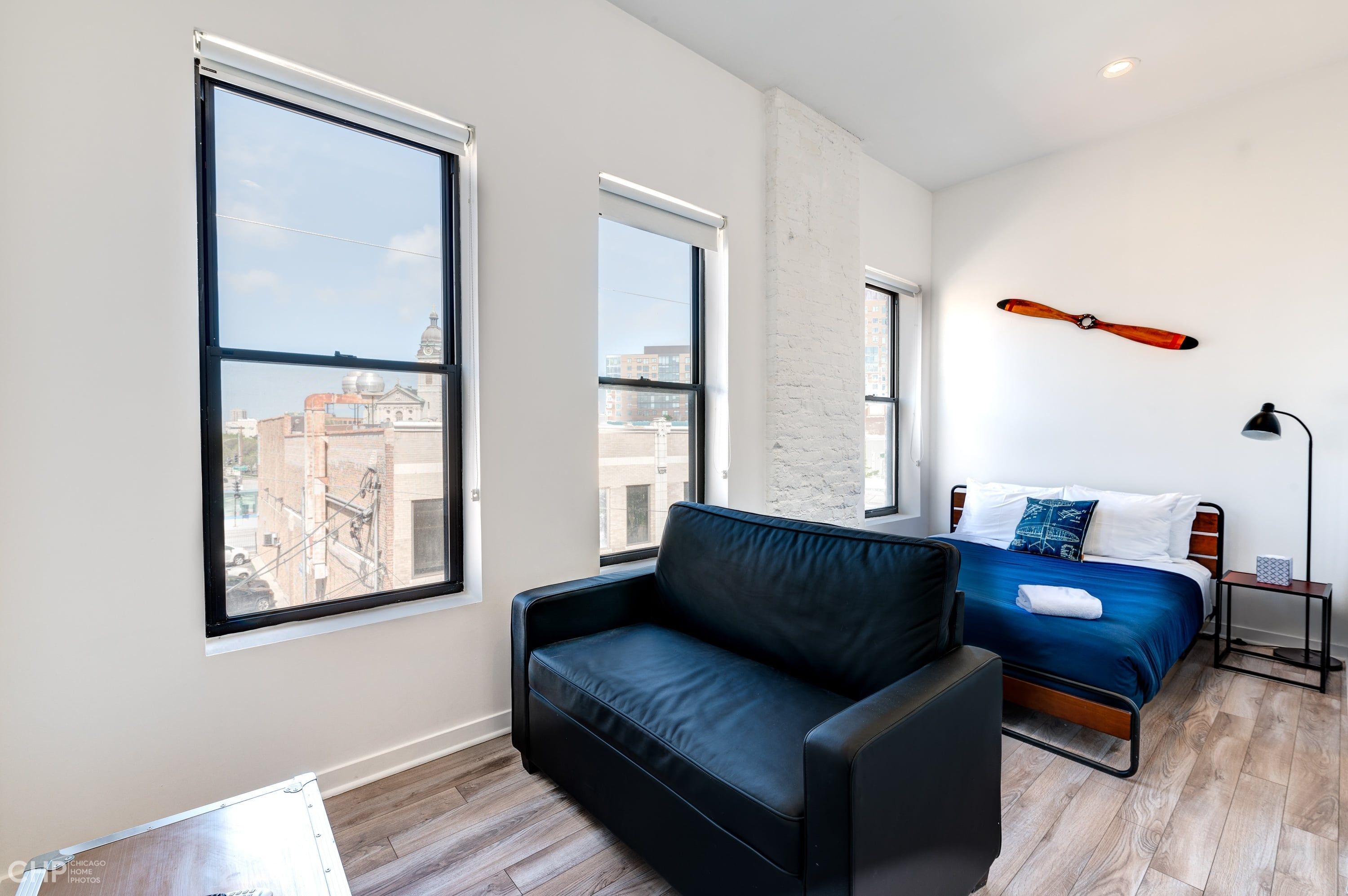 Een moderne kamer met een bed, een leren zwarte bank en grote ramen met uitzicht op de stad.