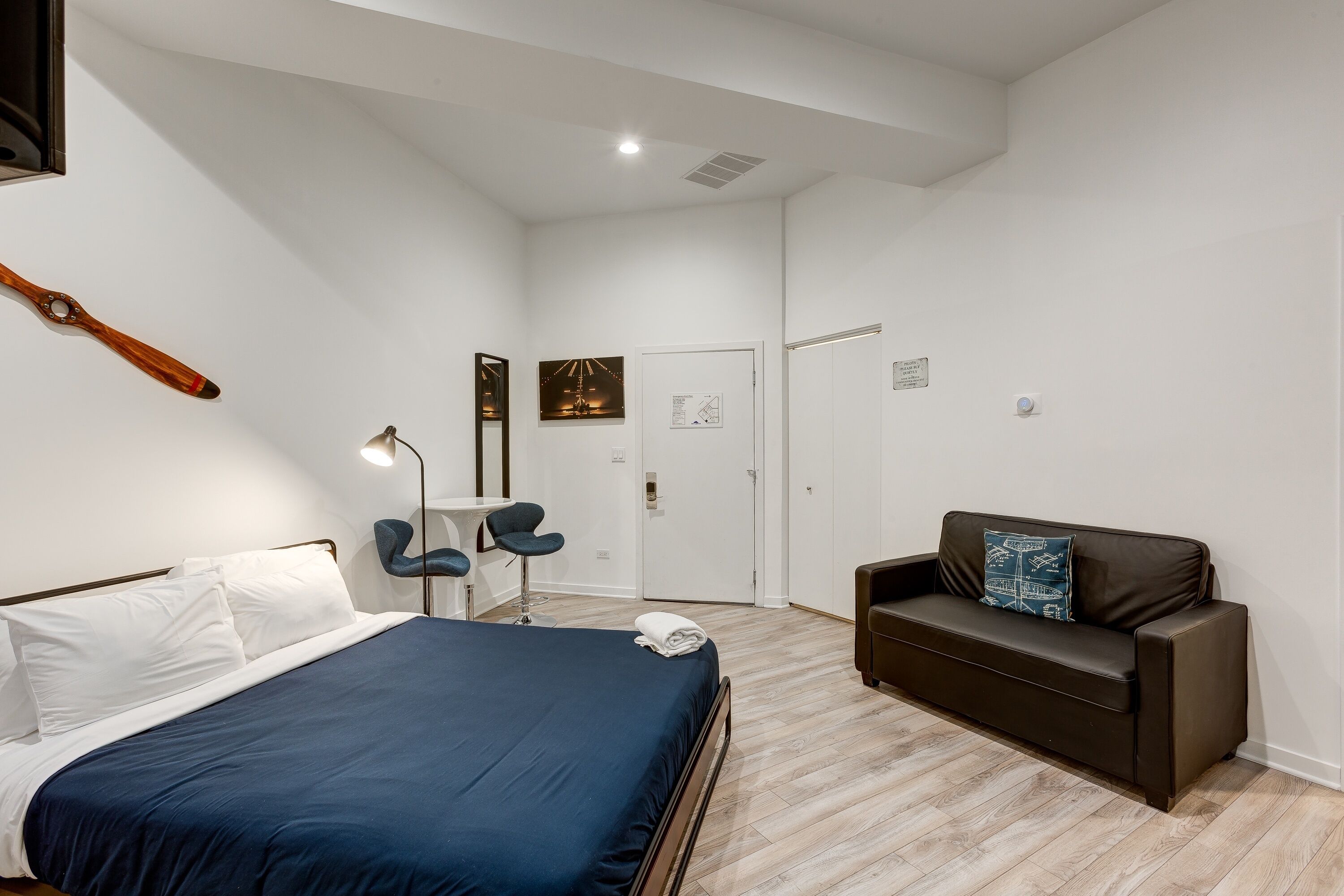 A modern hotel room with a bed, a dark brown sofa, a small table, and a chair.