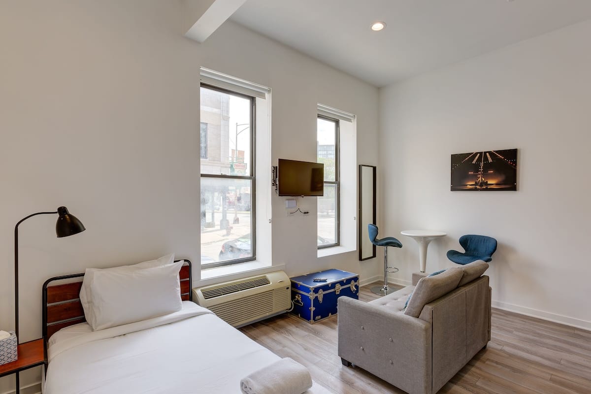 A hotel room with a bed, a sofa, a TV, a desk, and a window.