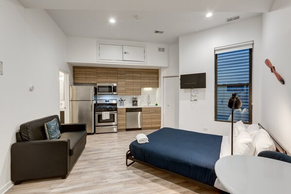 A compact room with a bed, a sofa, a small kitchen area, and a TV mounted on the wall. - Ground Floor Studios in Chicago by 747 Lofts (Chicago)