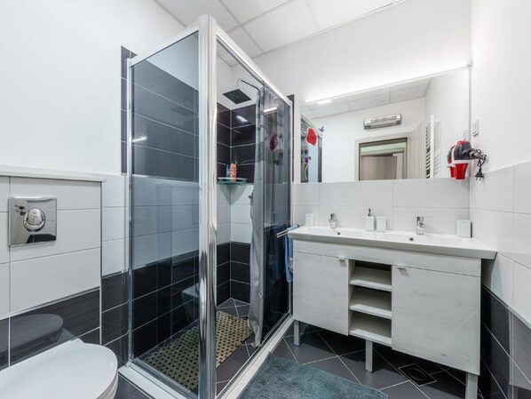 Een moderne badkamer met een douchecabine van glas, een witte wastafel en een spiegel erboven.