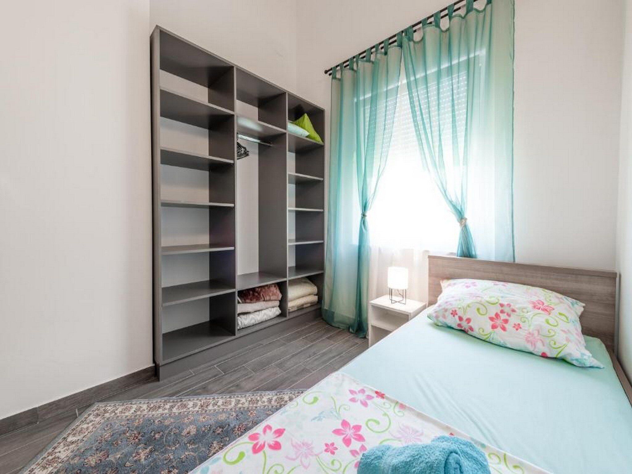 Ein Schlafzimmer mit Bett, Nachttisch, Kleiderschrank und einem Fenster mit Vorhängen.