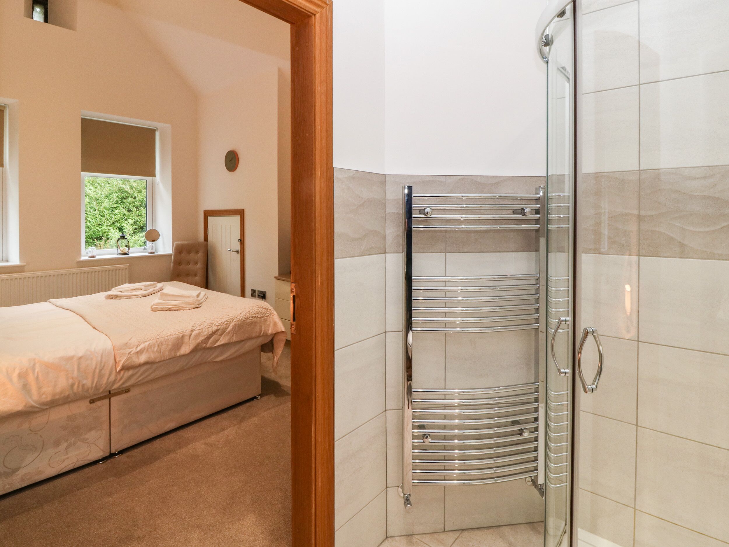 Un dormitorio con cama, mesita de noche, ventana y zona de ducha con puerta de cristal.