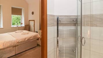 Un dormitorio con cama, mesita de noche, ventana y zona de ducha con puerta de cristal.