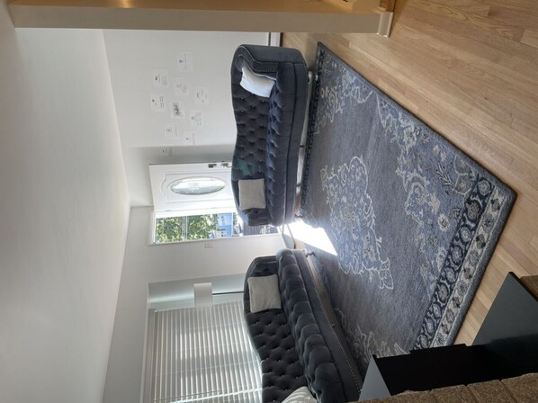A modern interior with a black tufted sofa, a patterned rug, and a wooden floor. - Home in Stratford (Stratford)