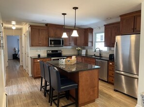 A modern kitchen with wooden cabinets, stainless steel appliances, and a central island with bar stools. - Home in Stratford (Stratford)