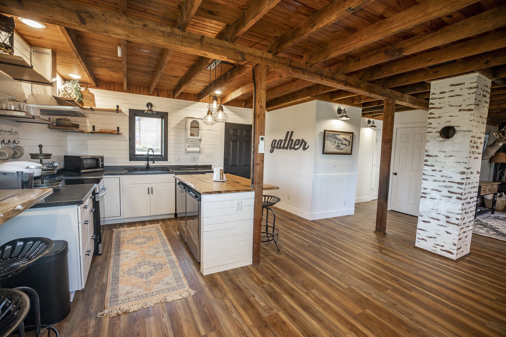 A spacious kitchen with wooden beams, a central island, and a 'gather' sign on the wall.