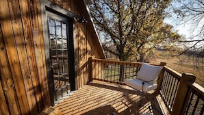 Une terrasse en bois avec un banc et une table, une porte et une vue sur les arbres.