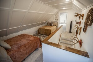 A loft bedroom with a sloped ceiling, a wooden bench, a bed with a brown quilt, and antler decorations on the wall. - The Guesthouse Getaway (Lindsborg)