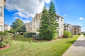 A residential building with multiple balconies, a well-maintained lawn, and a large evergreen tree in the foreground. - Harry's Mystical Hideaway in Gated Windsor Palms 15 minutes to Disney (Kissimmee)