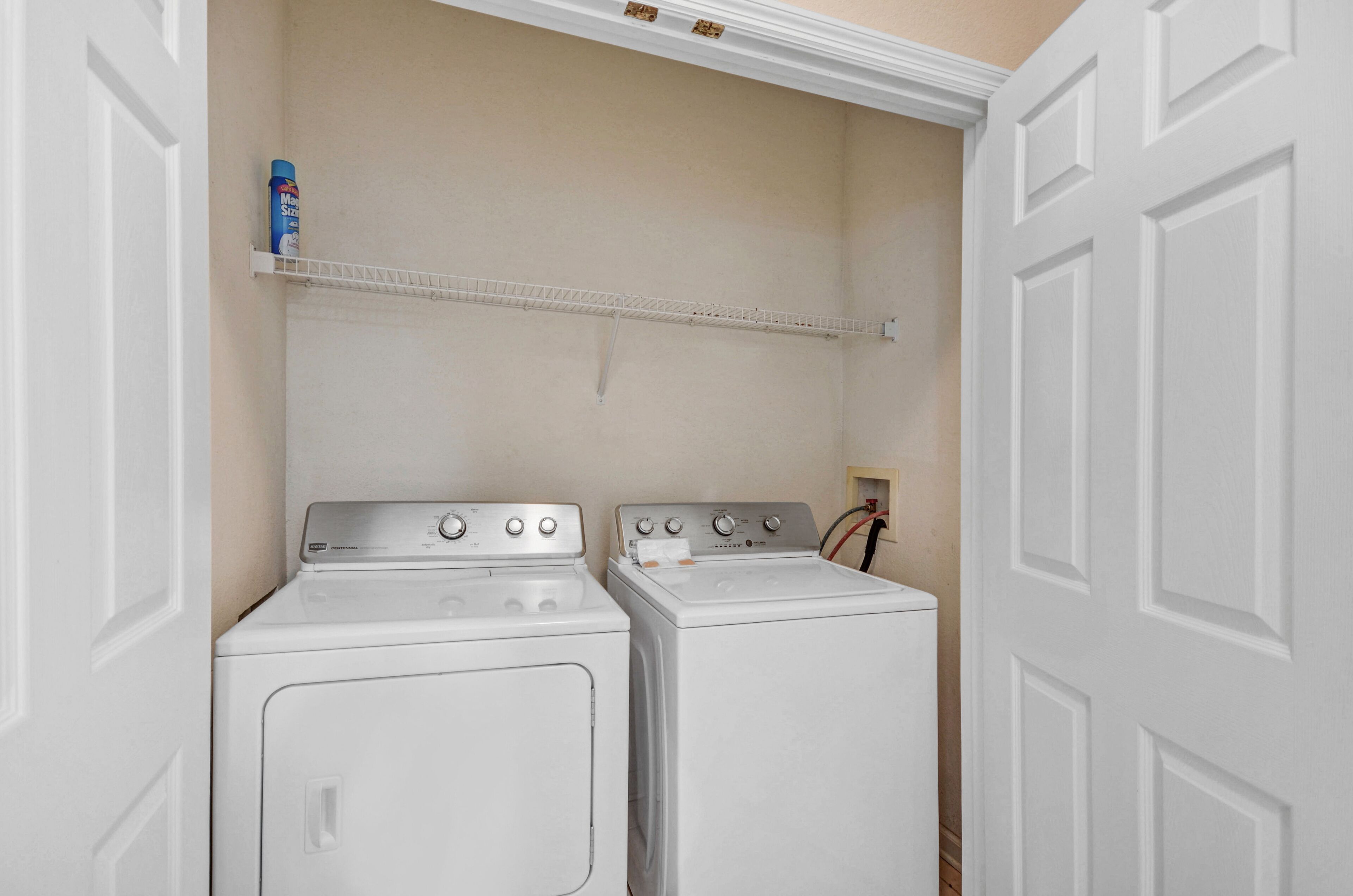 A laundry room with two stacked washers and dryers, a shelf above the dryers, and a door to the right.
