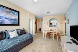 A living room with a sofa, a dining area with chairs, a TV, and a kitchen in the background. - Harry's Mystical Hideaway in Gated Windsor Palms 15 minutes to Disney (Kissimmee)