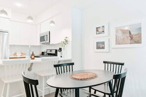 A modern kitchen with white cabinetry, a microwave, and a coffee machine. There is a dining area with a round table and four chairs.