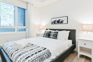 Ein Schlafzimmer mit Bett, Nachttisch, Fenster und einem an der Wand hängenden Bild.