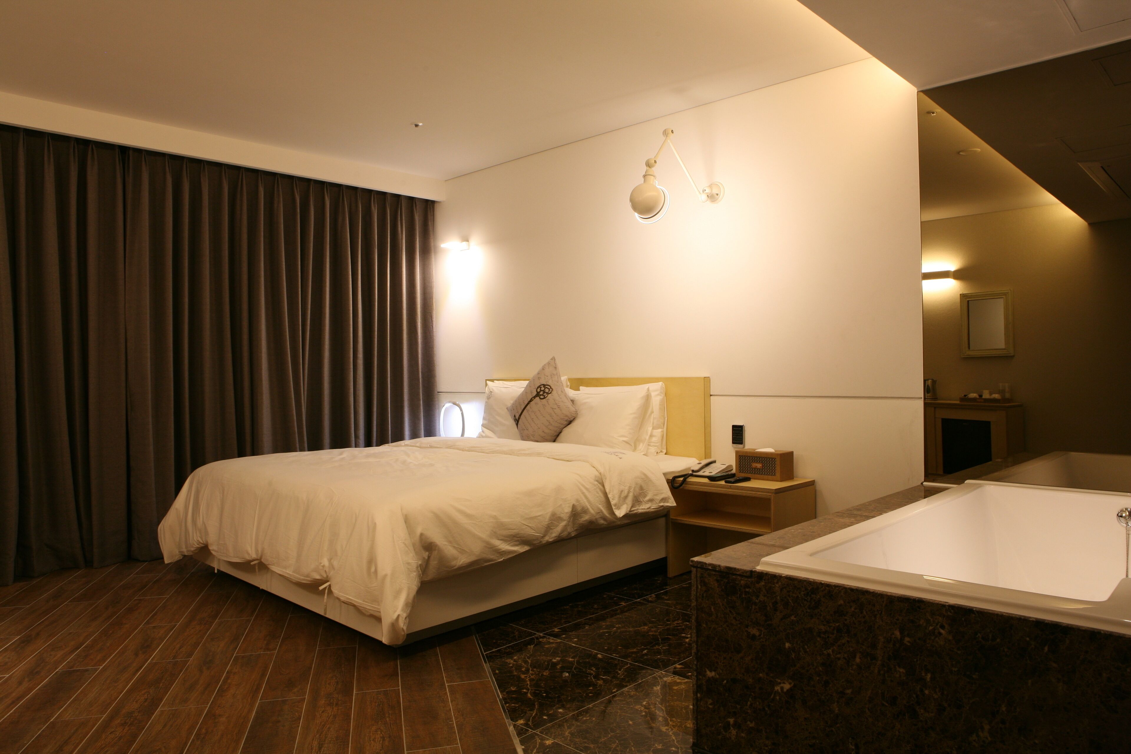 A modern hotel room with a large bed, a separate bathroom with a bathtub, and a wooden floor.