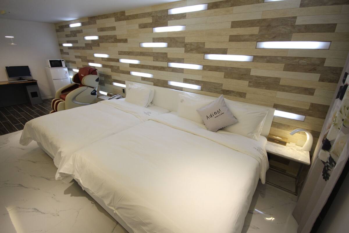 Habitación de hotel con una cama grande, una silla de masaje, un escritorio con computadora y un diseño de pared moderno.