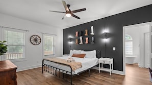 Une chambre à coucher comprenant un lit, des tables de chevet, un ventilateur de plafond et un luminaire fixé au mur.
