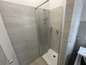 Een douchecabine met glazen wanden, een betegelde vloer en wanden, een handdouche en een muurkranen.