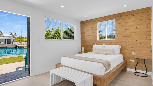 Ein Schlafzimmer mit einem Holzkopfteil, einem großen Bett, einer Bank und Blick auf einen Swimmingpool.